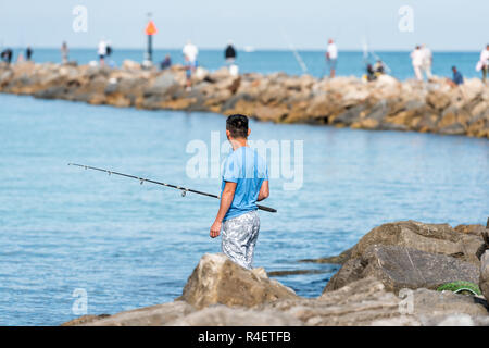 Venice, USA - April 29, 2018: Young man standing fisherman fishing on rocky pier in Florida retirement beach city, town, or village in gulf of Mexico  Stock Photo