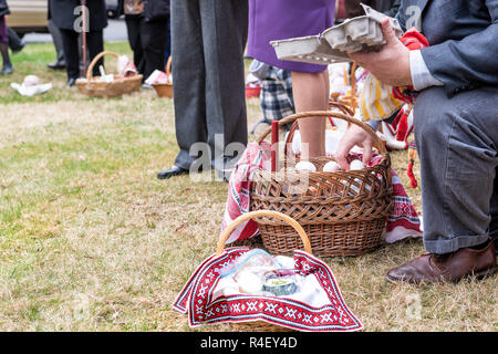 People man putting eggs from carton to Easter blessing basket, covered embroidered towel outside at church Stock Photo