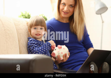 Child little girl arm putting coin in piggybank Stock Photo