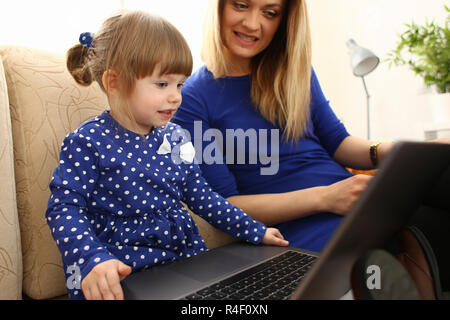 Cute little girl on couch with mom use laptop Stock Photo