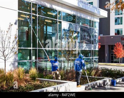 CHARLOTTE, NC, USA-11/21/18: Two men wash windows with attachments on long poles. Stock Photo