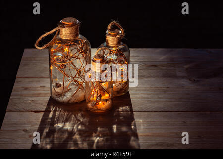 Bottles filled with lights, branches and snow standing on Outdoor Wooden Table Top at night Stock Photo