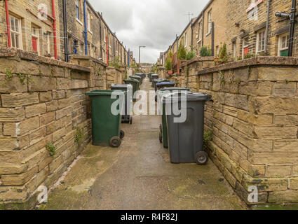 Two lines of wheelie bins line the alleyway between two rows of terraced houses in Saltaire, West Yorkshire Stock Photo