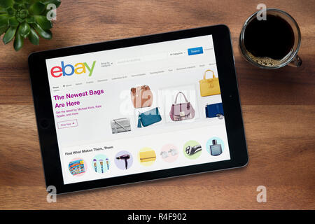 The website of ebay is seen on an iPad tablet, on a wooden table along with an espresso coffee and a house plant (Editorial use only). Stock Photo