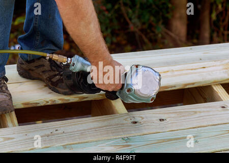 Man building a wooden patio with hammering screwing together beams close up of exterior timber decking. Stock Photo