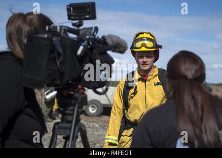 Local media reporters interview U.S. Air Force Senior Airman Grant Kopplin, a fire protection specialist assigned to the 673d Civil Engineer Squadron, during a controlled burn at the Infantry Platoon Battle Course on Joint Base Elmendorf-Richardson, Alaska, May 4, 2017. Controlled burns consume accumulated dry brush and grass thereby reducing the risk of wildfires. Kopplin is a native of Willard, Mo. Stock Photo