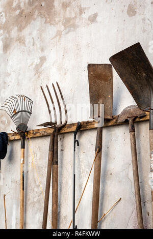 A collection of various used rusty garden tools hanging on weathered wall. Stock Photo