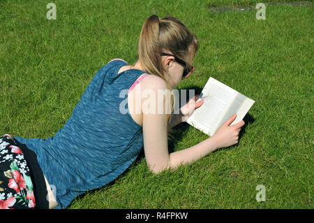 Teenage girl reading a book lying in the garden in summer. Stock Photo