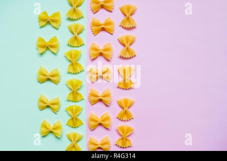 Frame from wheat pasta on pastel pink green background. Random pattern. Flat lay.Italian food concept.Bow tie Italian raw pasta fartalle pattern.Copy space. Diet and food concept. Stock Photo