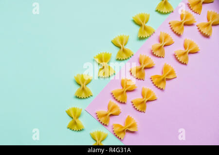 Frame from wheat pasta on pastel pink green background. Random pattern. Flat lay.Italian food concept.Bow tie Italian raw pasta fartalle pattern.Copy space. Diet and food concept. Stock Photo