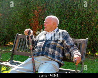 old man enjoys sitting on a bench in his garden Stock Photo