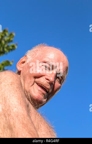 Tanned and fit senior man wearing blue swim trunks and a pair of