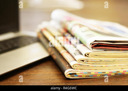 Newspapers and laptop. Pile of daily papers with news on computer. Pages with headlines, articles folded and stacked on keypad of electronic device Stock Photo