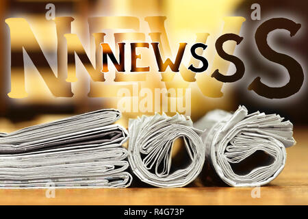 Fresh newspapers with latest news  folded and rolled on wooden table with blurred yellow background and multiple word News above the journals Stock Photo