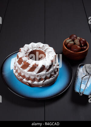 Delicious chestnut bundt cake using sweetened chestnut purée and chocolate chips, dusted with sugar, set on a blue plate, on a dark brown background Stock Photo