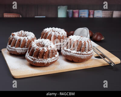 Miniature Chestnut Bundt Cakes with Chocolate Chips on a bamboo cutting board, on a dark brown background Stock Photo