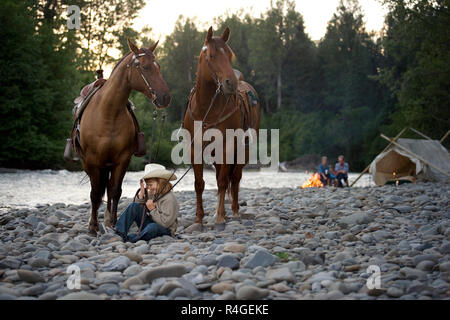 Girl sitting on riverbed holding horses reins Stock Photo