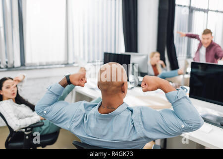 back view of african american man showing biceps and young colleagues having fun in office Stock Photo
