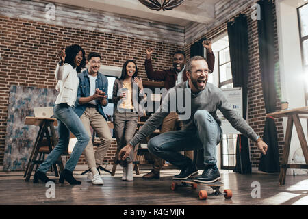 group of multiethnic coworkers having fun with skateboard in loft office Stock Photo