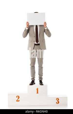 businessman hiding behind empty card while standing on winners podium isolated on white Stock Photo