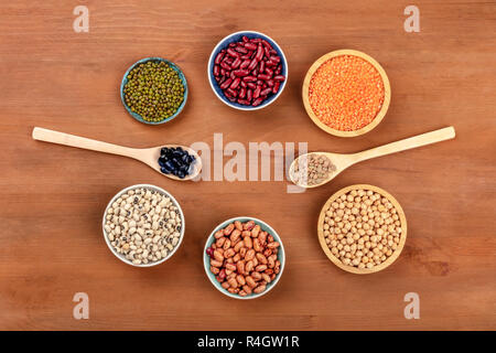 Various types of legumes, shot from the top on a dark rustic wooden background with a place for text. Red kidney, pinto, and black beans, lentils, chi