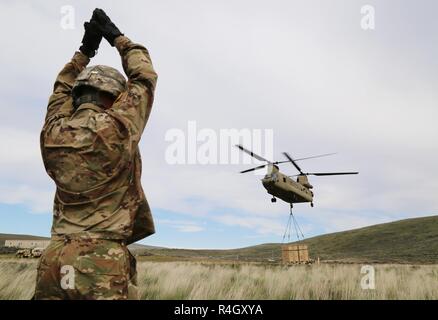 U.S. Army Pvt. Travis Botson, 92nd Chemical Company, 33rd Chemical Battalion, 48th Chemical Brigade, gives arm and hand signals to a CH-47 Chinook during a sling load operation at the Yakima Training Center, Yakima, Wash., May 5, 2017. Sling load operations allow units to accomplish their mission by rapidly relocating supplies and equipment, bypassing surface obstacles. Stock Photo