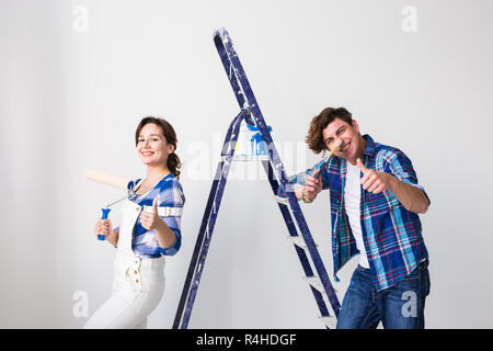 Repair, renovation and love couple concept - young man and woman in love and painting the wall, showing thumbs up. Stock Photo