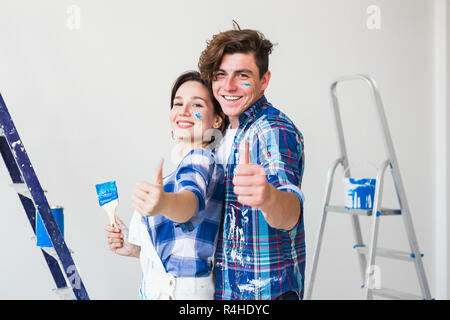Repair, renovation and love couple concept - young man and woman in love and painting the wall, showing thumbs up. Stock Photo