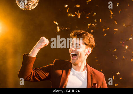happy young man celebrating under falling confetti on black Stock Photo