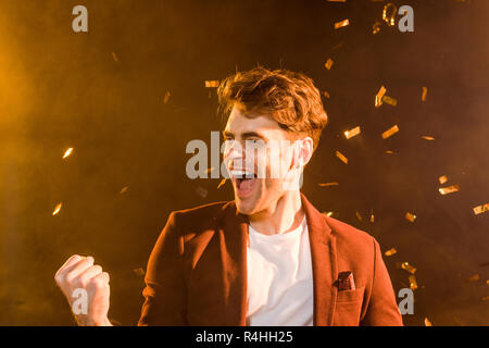 celebrating young man under falling confetti on black Stock Photo