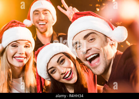 close-up shot of group of friends in santa hats celebrating new year and looking at camera Stock Photo