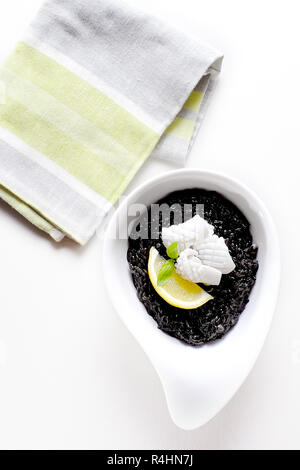 Squid ink black risotto on white plate background top view Stock Photo