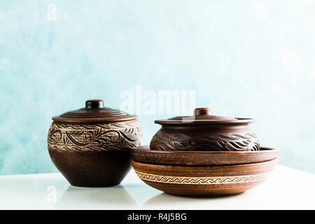 pots and plates of clay on a white table and a blue background. clay pottery kitchen utensils made by hand. red clay tableware Stock Photo