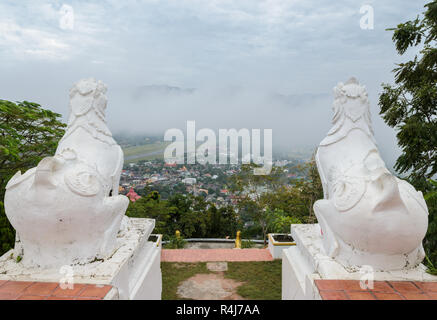 Lion statue at Wat Phra That Doi Kong Mu with city view of Mae Hong Son in the mist, Thailand Stock Photo