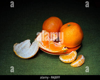 Mandarin or clementine oranges, dark still life on green. Light painting technique. Three fruit, one part peeled. Stock Photo