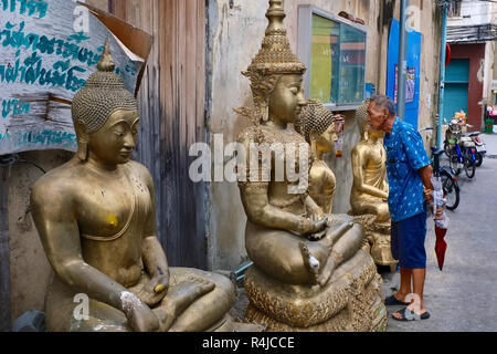 Outside a factory for Buddha statues in Bamrung Muang Road in Bangkok, Thailand, a man looks inensely at a statue placed outside for delivery Stock Photo