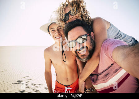 Happy family outdoor at the beach during a vacation. Tourists taking selfie in happiness together in holiday with sand dunes resort in background. Enj Stock Photo