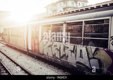 A train with closed doors waiting for passengers at the railway station. Street art and urban culture painted on the tube, Sunlight in background Stock Photo