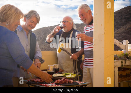 people in friendship mature couples have together a barbecue at home drinking and eating enjoying the retired life and the friends day - celebration a Stock Photo
