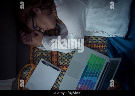 night shot and situation with tired woman worker sleeping on the sofa at home with open laptop and white paper empty of notes - stress and technology  Stock Photo