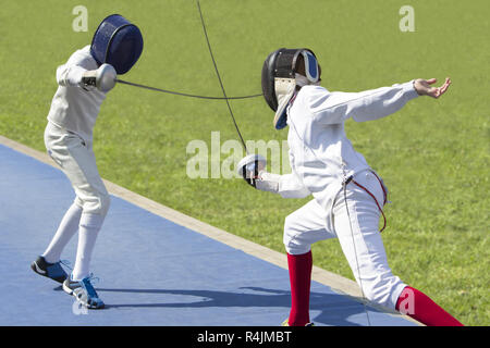 Two young man fencing athletes fight on outdoor playground Stock Photo