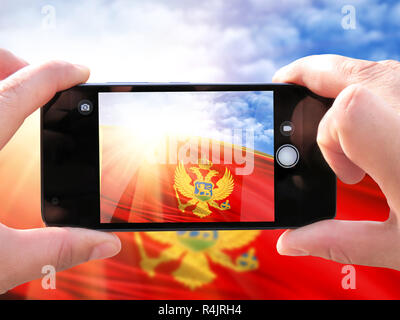 The concept of tourism and travel. The hands of men make a phone photograph of the flag of Montenegro. On the smartphone close-up image of the flag. P Stock Photo