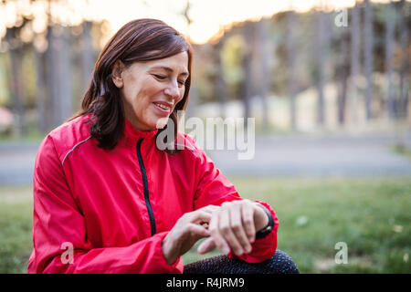 A female runner outdoors in autumn nature, checking the time. Stock Photo