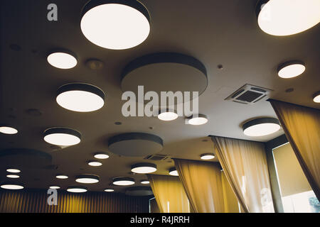 big grey ivory hexagons with light inside is on ceiling with classic office squares in Modern Design Studio, large hexagon chandelier against geometric ceiling as a decor modern element. Stock Photo