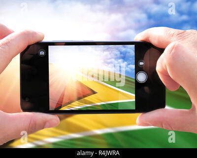 The concept of tourism and travel. The hands of men make a phone photograph of the flag of Guyana. On the smartphone close-up image of the flag. Photo Stock Photo