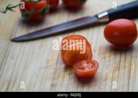 Red sliced Cocktail Tomatoes and a Knife on a wooden Table. Stock Photo
