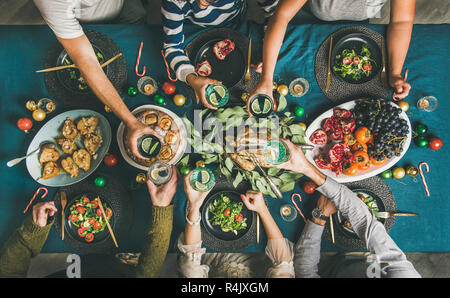Company of friends gathering for Christmas or New Year party dinner at festive table. Flat-lay of human hands holding glasses with drinks, feasting an Stock Photo