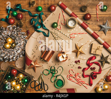 Flat-lay of hot chocolate drink with toasted marshmallows, Christmas decorations, ribbons, gift paper, glittering balls, candy canes over wooden backg Stock Photo
