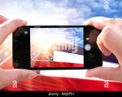 The concept of tourism and travel. The hands of men make a phone photograph of the flag State of Mississippi. On the smartphone close-up image of the  Stock Photo