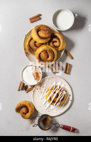 Homemade pumpkin cinnamon bun rolls sweet autumn baked dessert with cream cheese sauce in spotted ceramic plates with cinnamon sticks and vintage siev Stock Photo